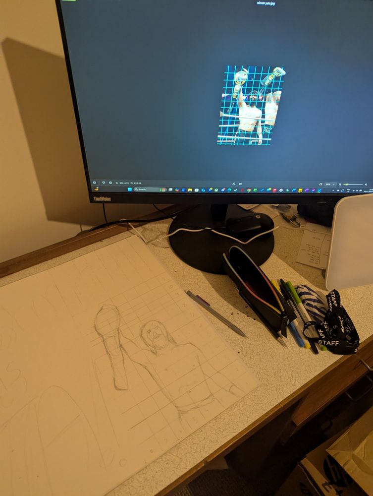 A display with a picture of wrestler Wheeler Yuta holding a belt, that has been overlaid with a reference grid. On the table, a rough outline of the same image on the edge of what will be a wrestling sign.