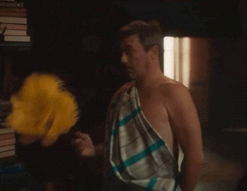 Gif of Gabriel as 'Jim' with a yellow feather duster in Aziraphale's bookshop