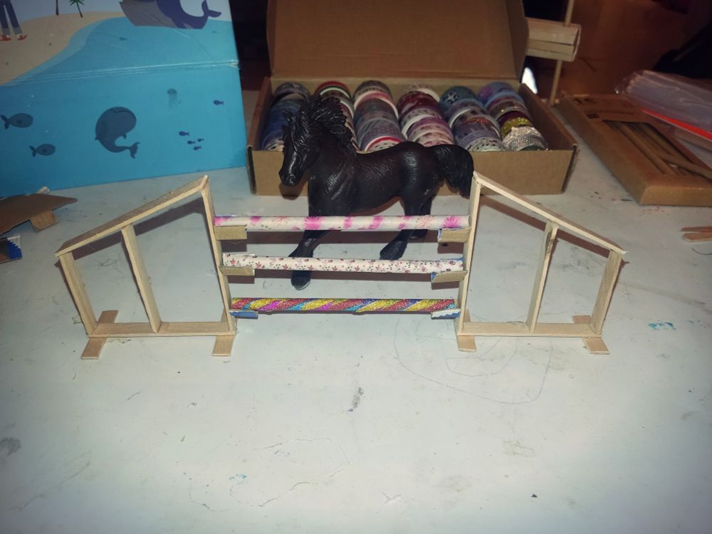 Ein schwarzes Schleichpferd steht hinter einem Hindernis, das aus Eisstilen und Papier-Strohhalmen gebastelt ist.