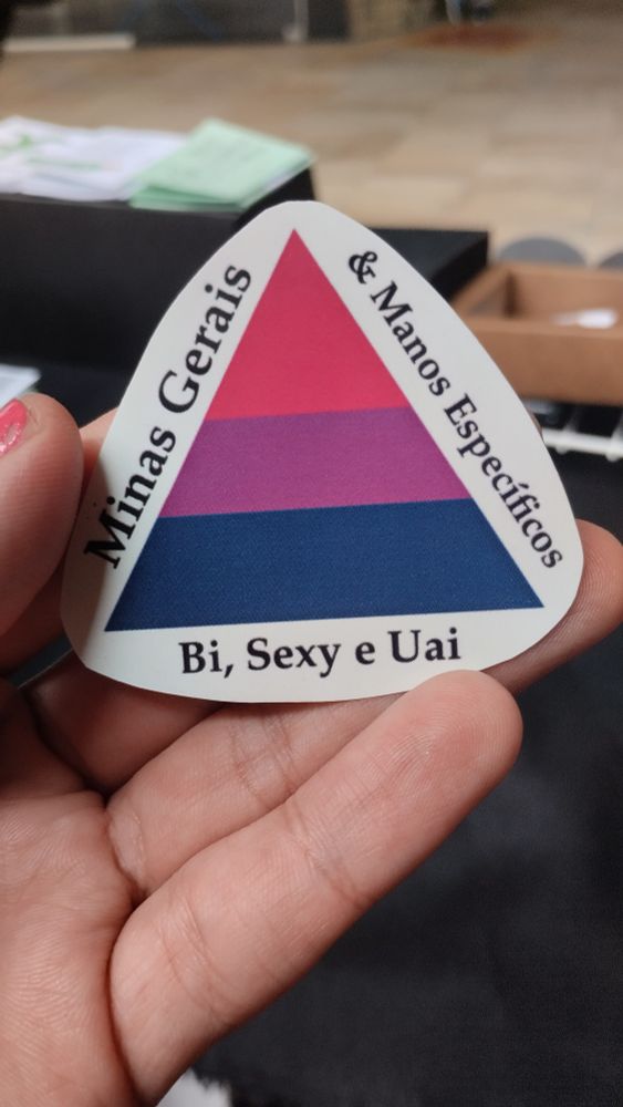 Adesivo com o triângulo da bandeira de minas gerais, mas com as cores da bandeira bissexual (vermelho, roxo e azul) e em torno do triângulo a frase "minas gerais e manos específicos. Bi sexy e uai"