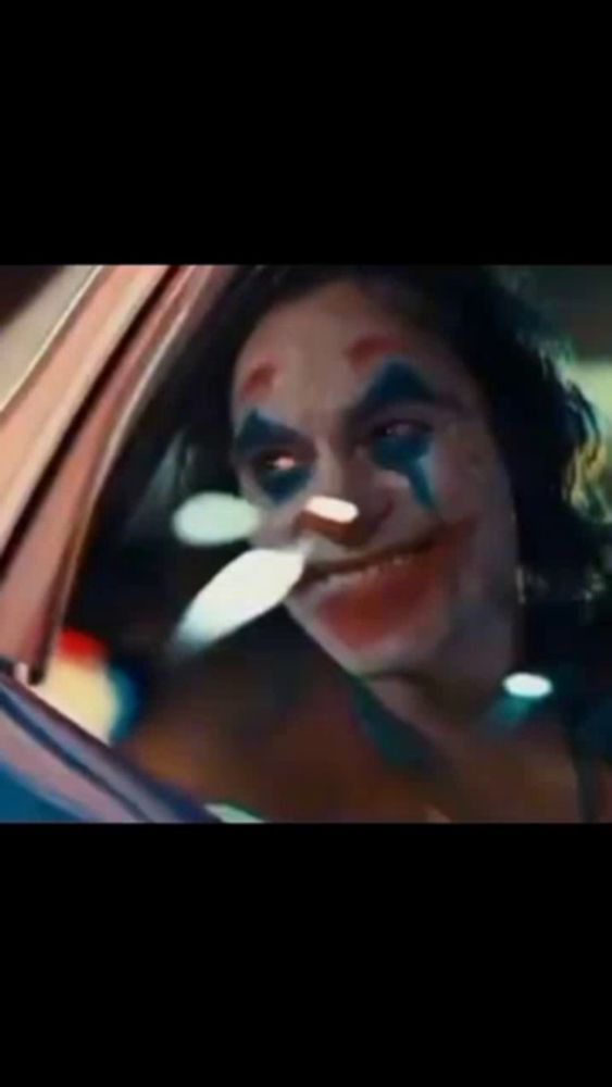 the joker is looking out of the window of a car .