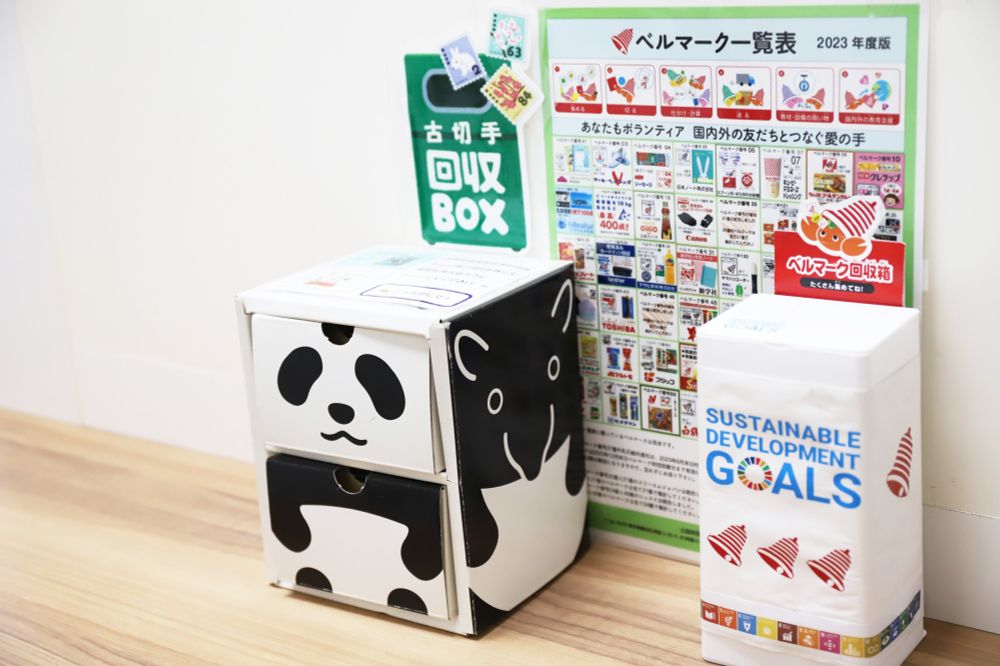 白いプラスチック製のベルマークの回収BOXと、パンダとバクのキャラクターが描かれた古切手の改修BOXの写真
