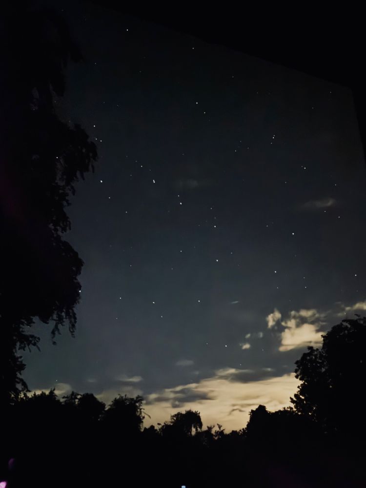 A view of the Plough or Big Dipper in the night sky with a mass of clouds in the lower right corner with light reflecting off of them. 