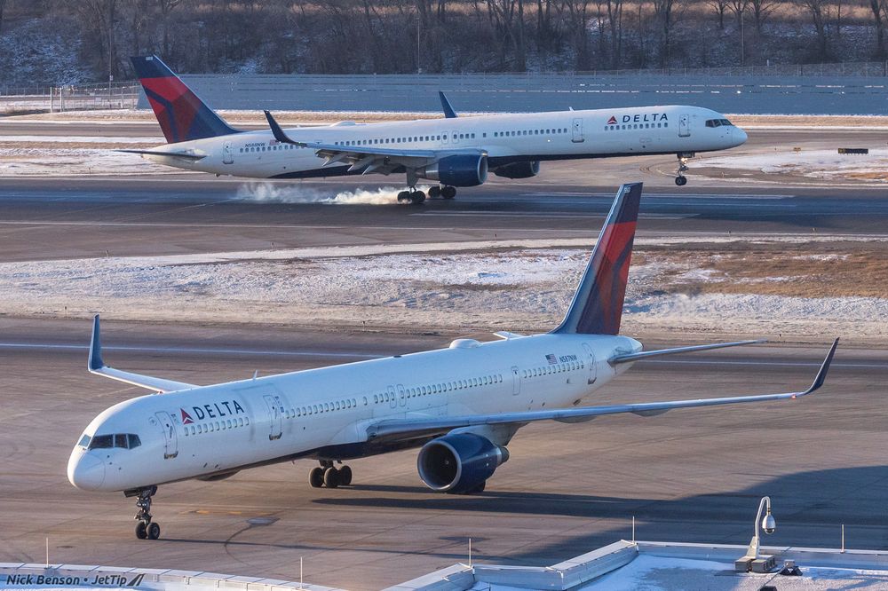 A pair of Delta 757-300s; one has just touched down in the background, with a puff of smoke coming off of the main gear.