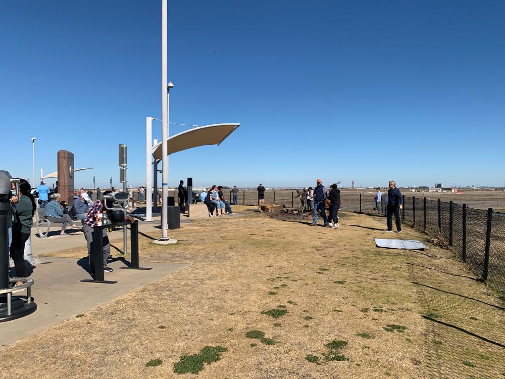 A small crowd of people enjoying DFW’s aircraft viewing area, Founder’s Plaza.