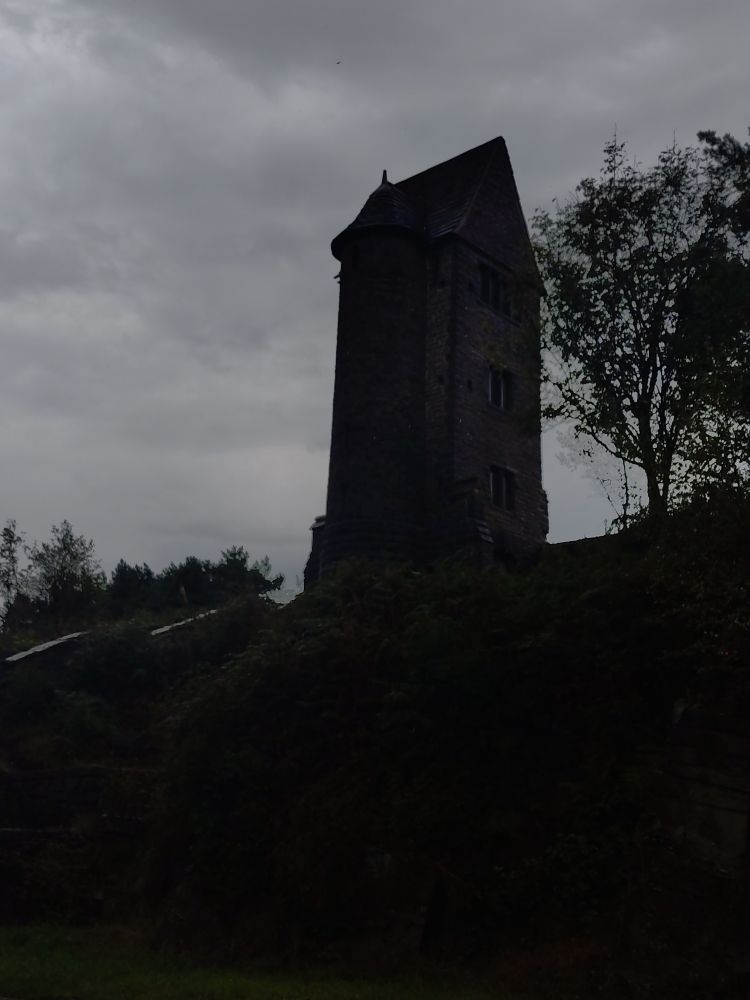 A shot of the pigeon tower from a bit further down the hill. It is almost completely silhouetted against a cloudy grey sky.