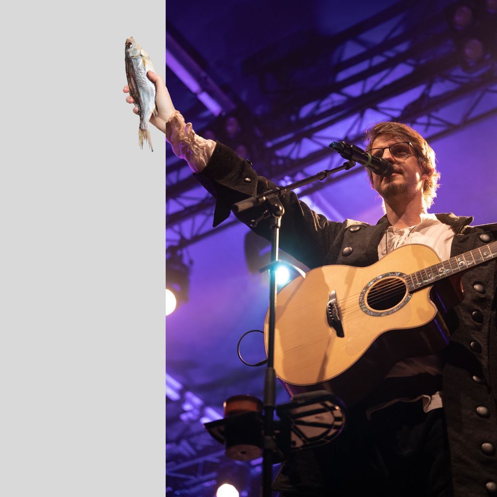 A picture of JD from Castlefest, wearing his dandy pirate costume, right arm extended out towards the audience and look! He's offering them some kind of dried fish, clutched in his right hand and breaking out the side of the frame. Incredible.