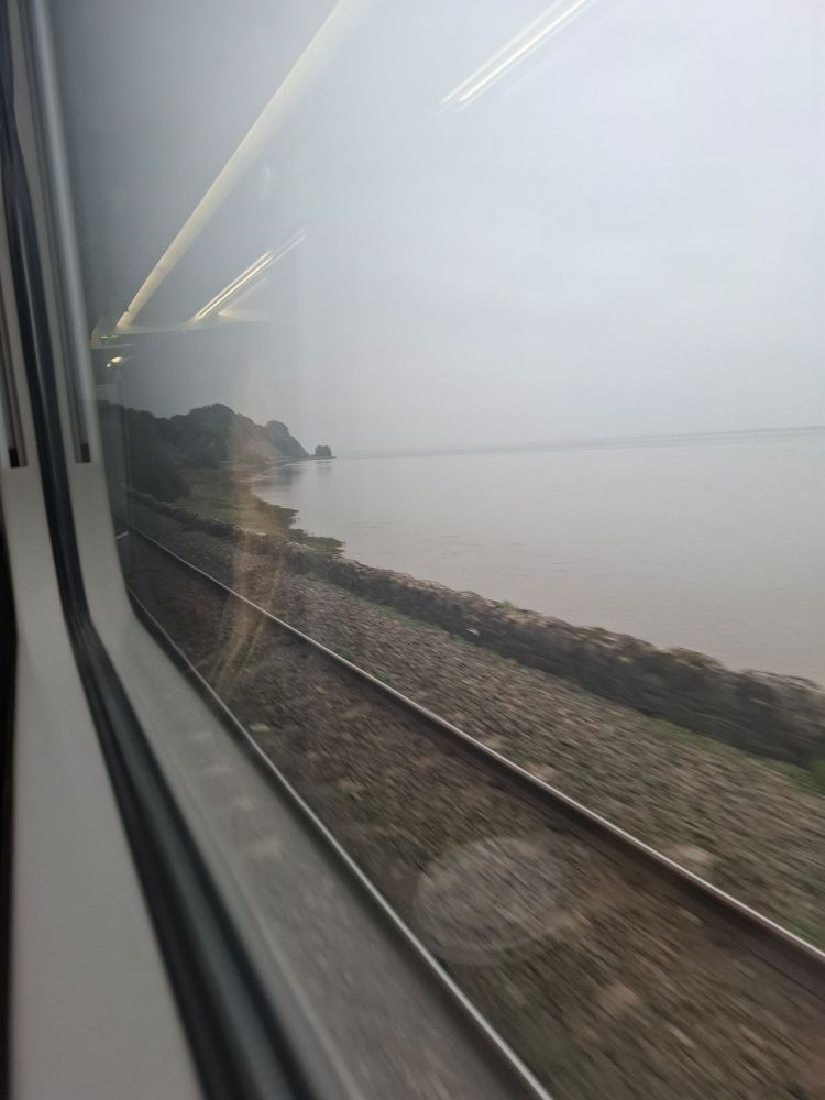 photograph from a train window, showing train tracks going up the coast. on the right is the edge of a river