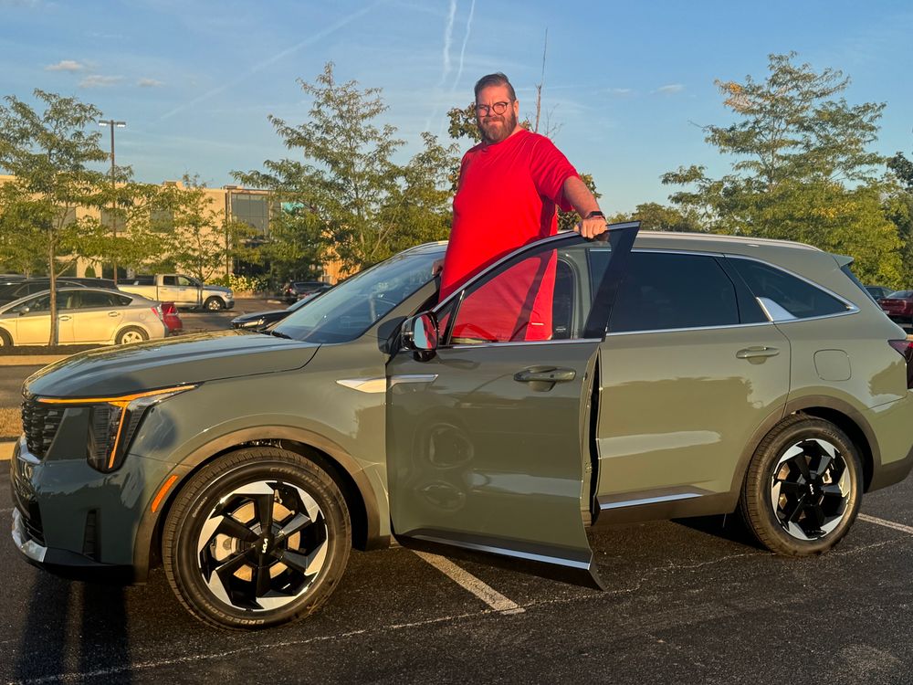 An olive green Kia Sorento with me standing behind the driver’s side open door. 
