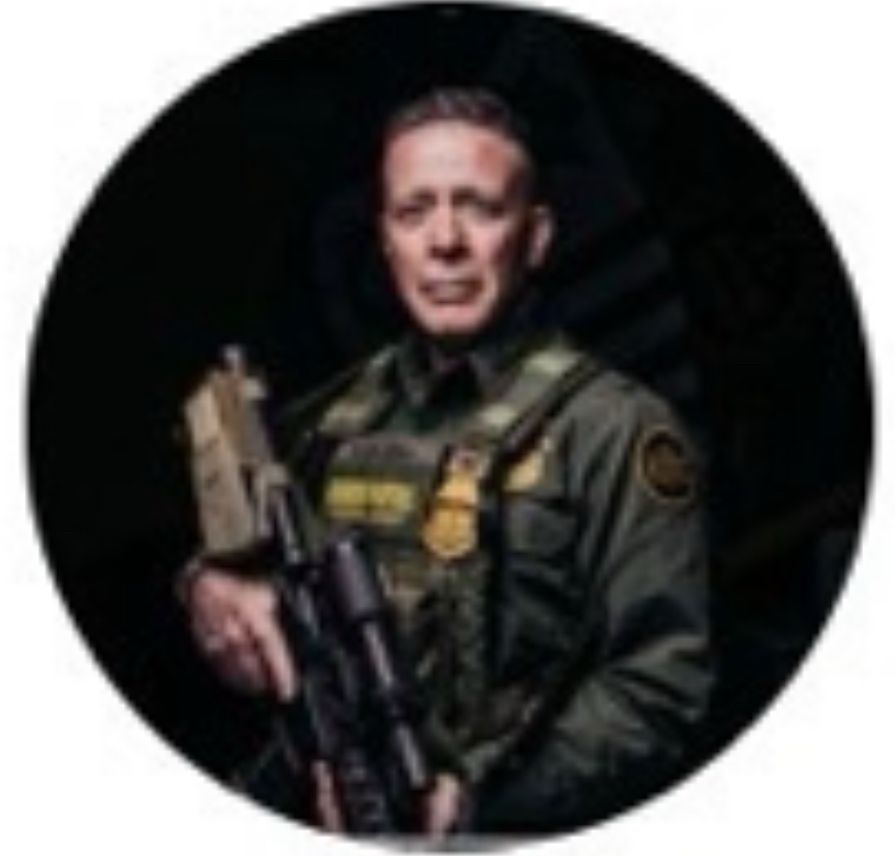 Avatar of Dan Bovino, a picture of himself in full combat gear holding a semi-automatic (?) rifle. 