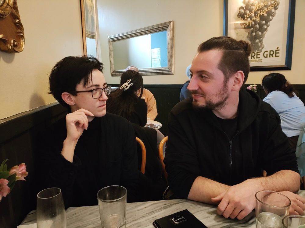 pic of my bfs out to eat, they're looking at each other, they're both dressed in dark clothes, there may or may not be sexual tension