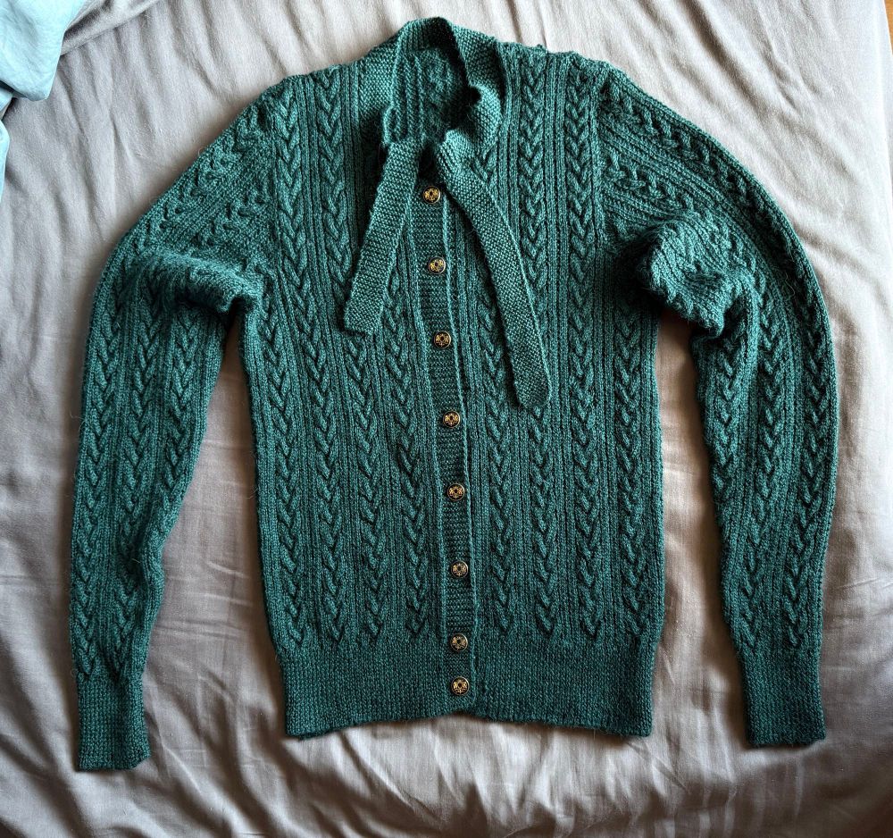 A green cable-knit cardigan with black and gold buttons 
