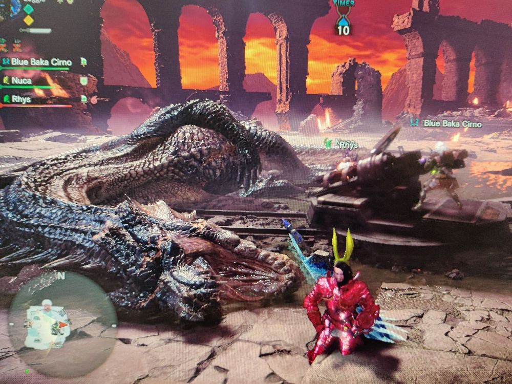 A hunter in pink armor and yellow bunny ears kneeling beside a slain Fatalis in Monster Hunter World: Iceborne