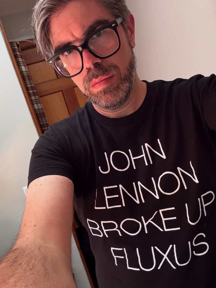 Black t shirt that says “John Lennon Broke Up Fluxus.” 