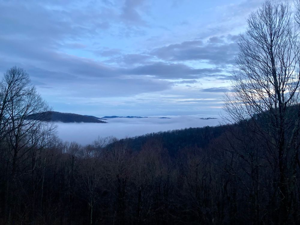 view from a north carolina balcony: mountaintops peek through the clouds, framed by trees and miscellaneous wilderness 