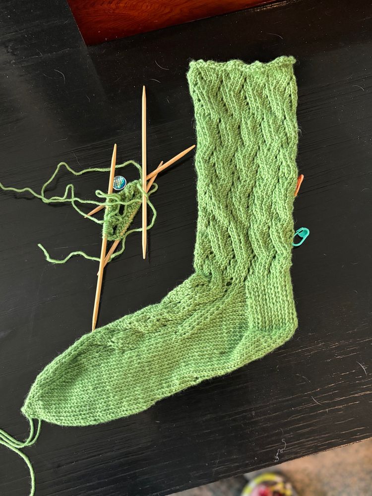 One green knitted sock completed but unfinished and unblocked and another sock cast on double pointed needles. 