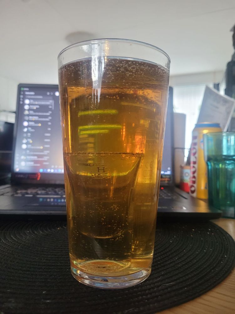 A pint of Obolon Premium beer with a shotglass of Propeller-rum in it on a dinner table. On the background an empty Obolon beer can, a laptop and a large drinking glass
