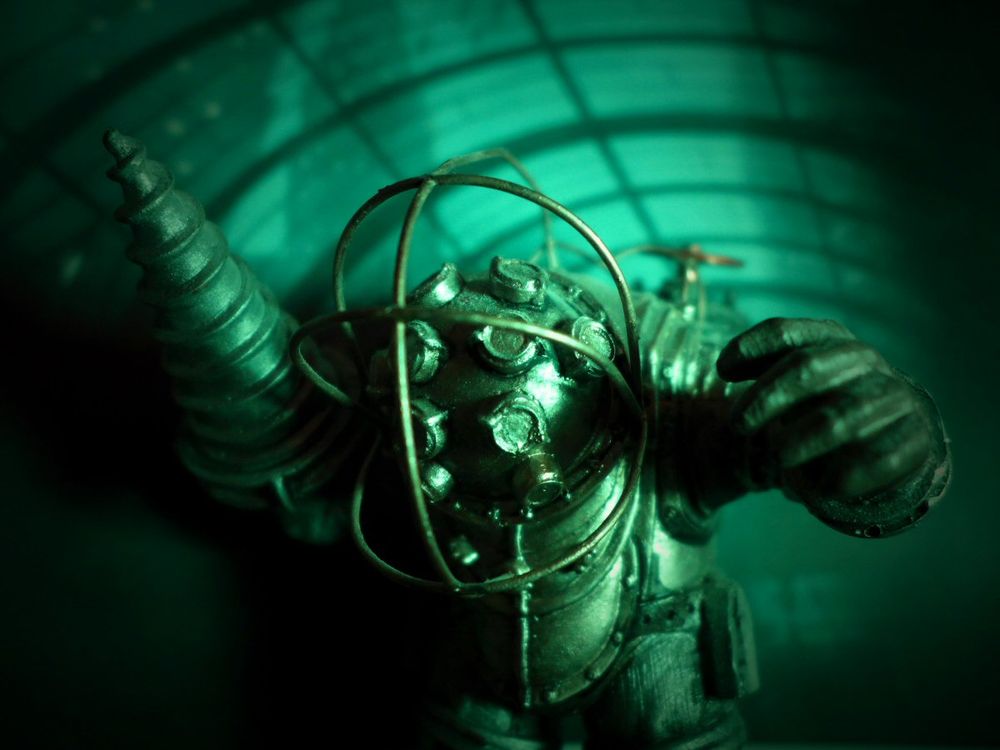 A Big Daddy figurine from Bioshock - bathed in green light and posed against a printed paper backdrop of Rapture.
