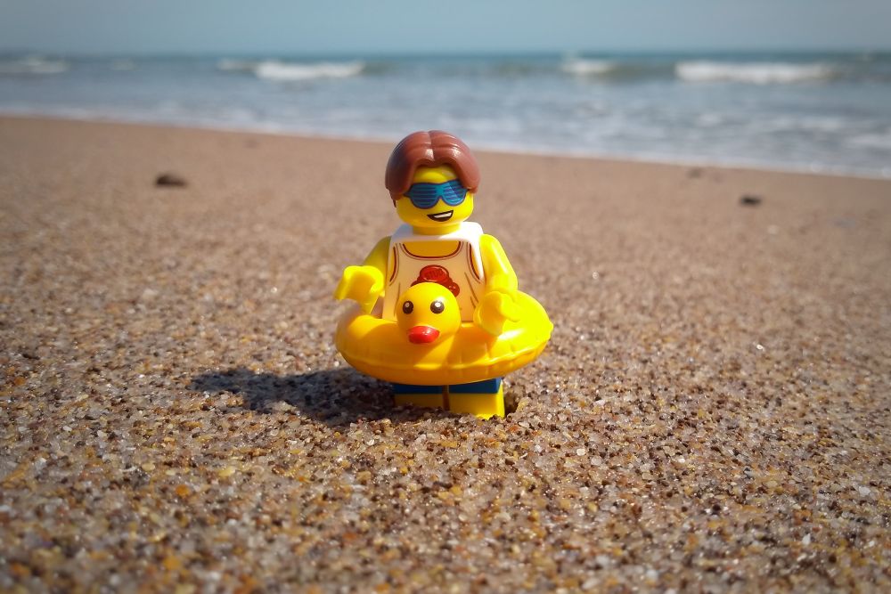 A cool dude Lego mini figure on a sunny beach, with an inflatable duck around his waist. Taken on Warkworth beach, Northumberland.
