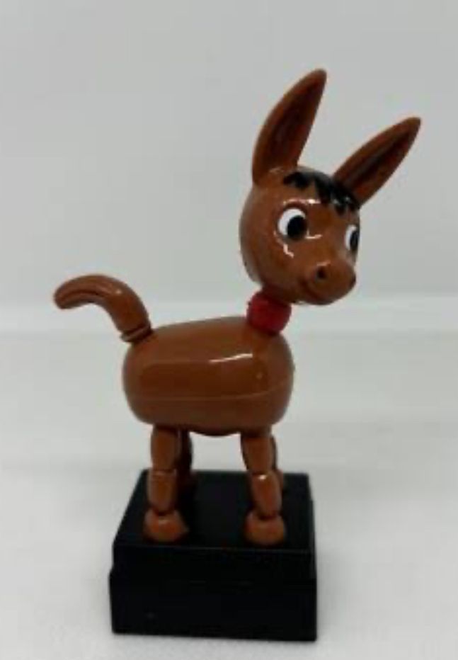 a small brown plastic donkey toy sitting on a black base. when you push underneath the base of the toy, elastic inside the donkey makes the toy collapse 