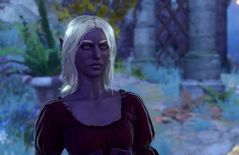A screenshot from Baldur’s Gate 3 depicting a young, drow elf woman with long white hair, purple skin with freckles, and red eyes wearing a burgundy blouse. 