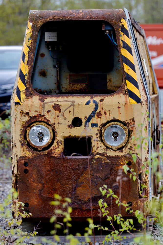 Ein angerosteter alter Grubenwagen, davor Gestrüpp