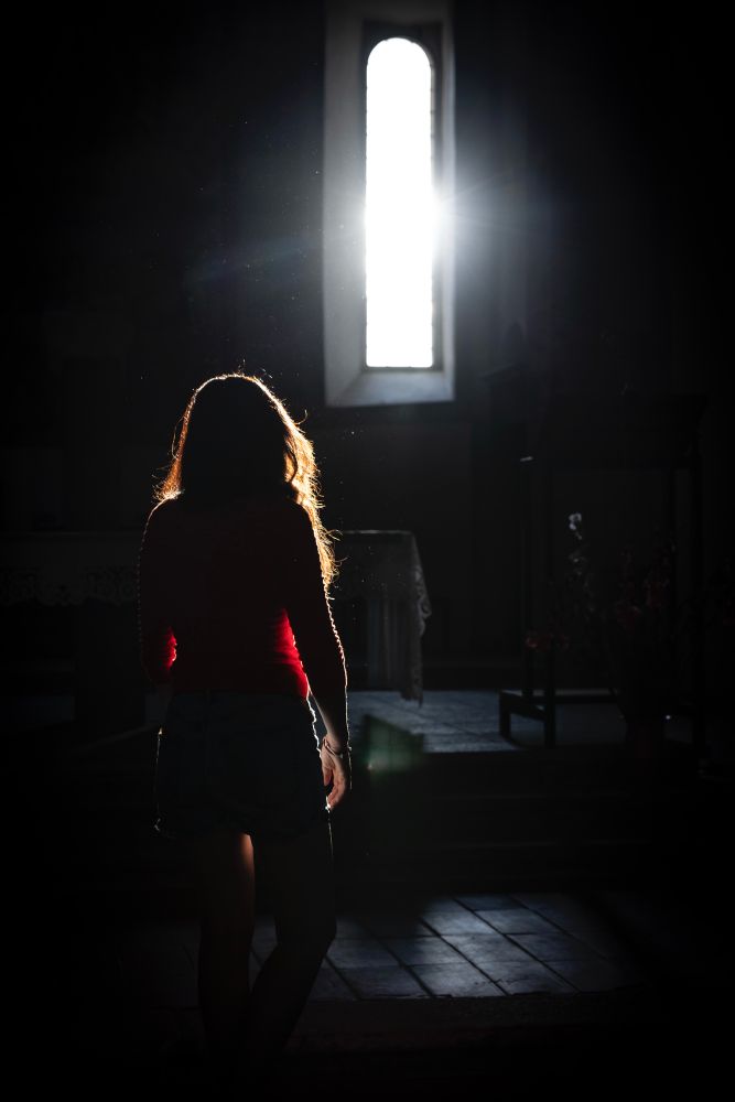 Eine Person in einem dunklen Raum, die durch das Sonnenlicht aus einem Fenster angestrahlt wird.