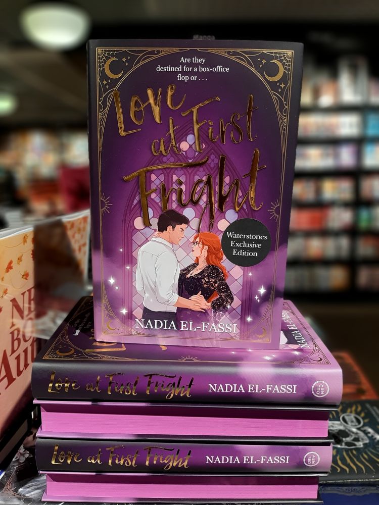 A pile of the book in a bookshop, some turned to show off the brilliant purple sprayed edge spredges.
