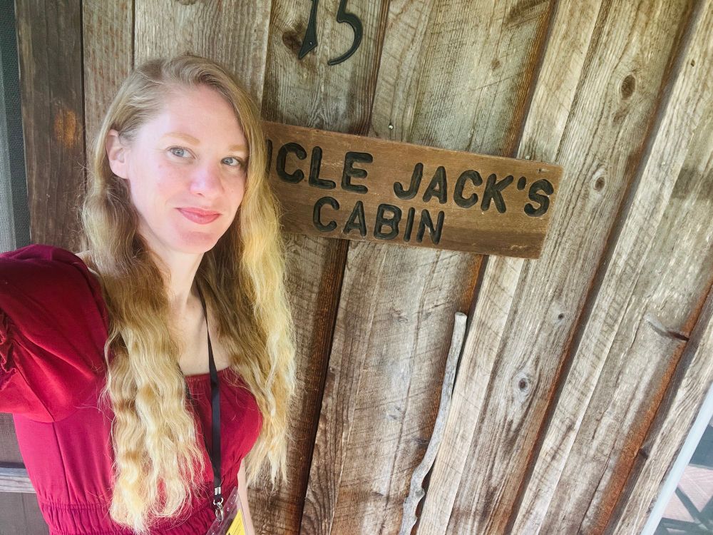 Me in a red sundress taking a selfie in front of a rustic cabin