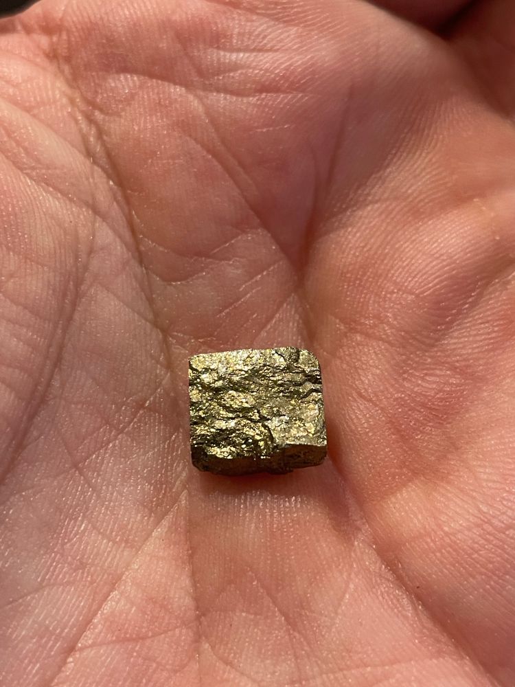 A hand holding a shiny metal rock. Is it gold?