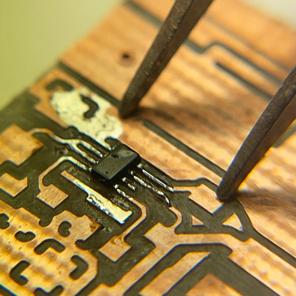 Close view of the soldered IC, about 2x1mm in size, with 8 pins. Tips of the tweezers beside it. Smol chip, yep.