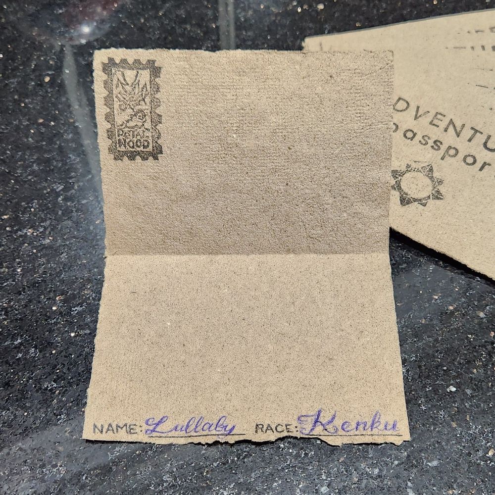 Handmade "adventure passports" folded open: a stamp at the top says Petalwood, and the text at the bottom says Name: Lullaby, and Race: Kenku.