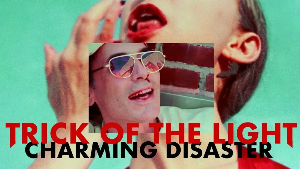 The cover image for Trick of the Light. In the foreground, Jeff Morris’ face is seen in a small rectangle, wearing an expression of awe, sunglasses, and a bloody nose. The background features Ellia Bisker from the nose to neck, mouth open to reveal fangs. Her hand is posed as if she’s tasting Jeff’s blood from her fingertips.