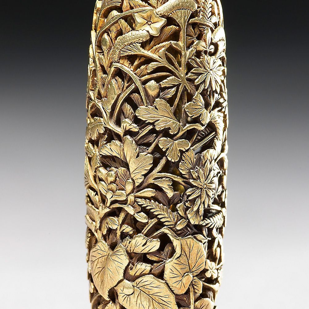 A Japanese ojime bead in gold intricately carved with autumnal leaves and flowers