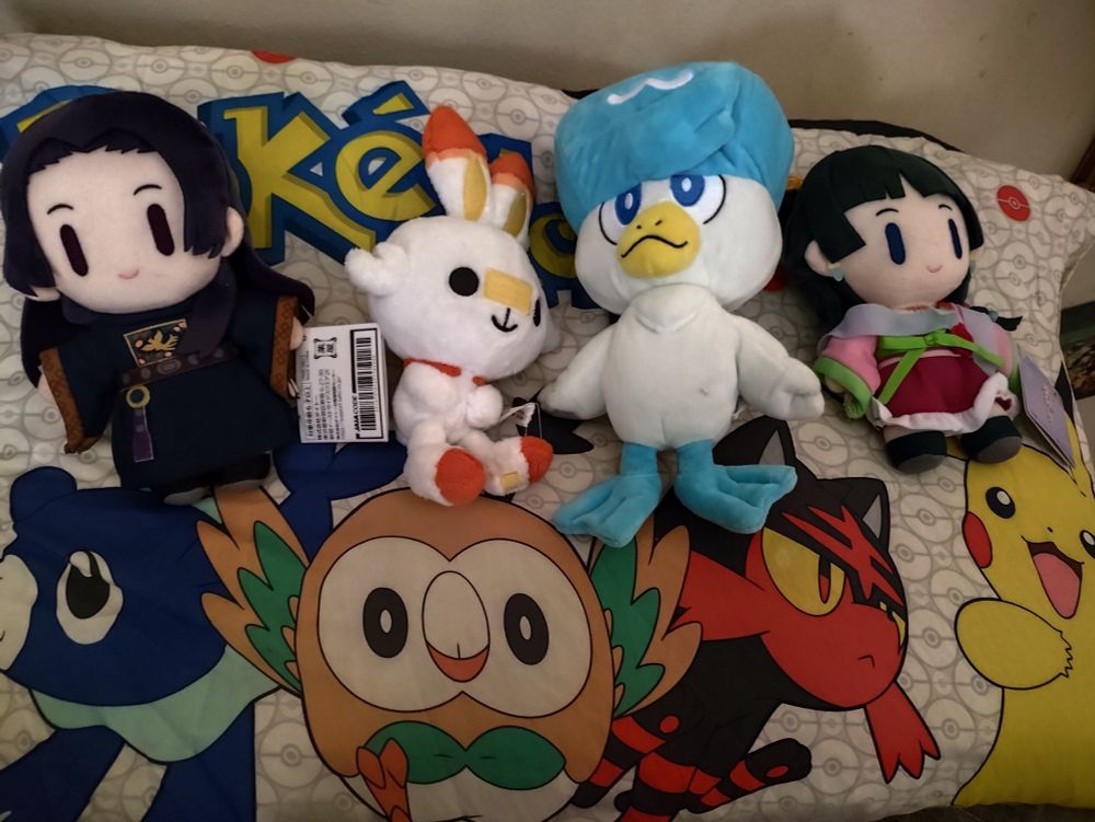 Almohada con funda de Pokémon con Popplio, Rowlett, Litten y Pikachu. Encima, peluches de Scorbunny y Quaxly, además de Maomao y Jinshi de Los Diarios de la Boticaria.
