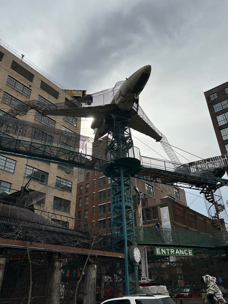 The front of the City Museum—and old brick buildings with a huge climbing structure for kids, including an entire airplane. Quixley (a plush zebra) looks on from the corner of the frame. 