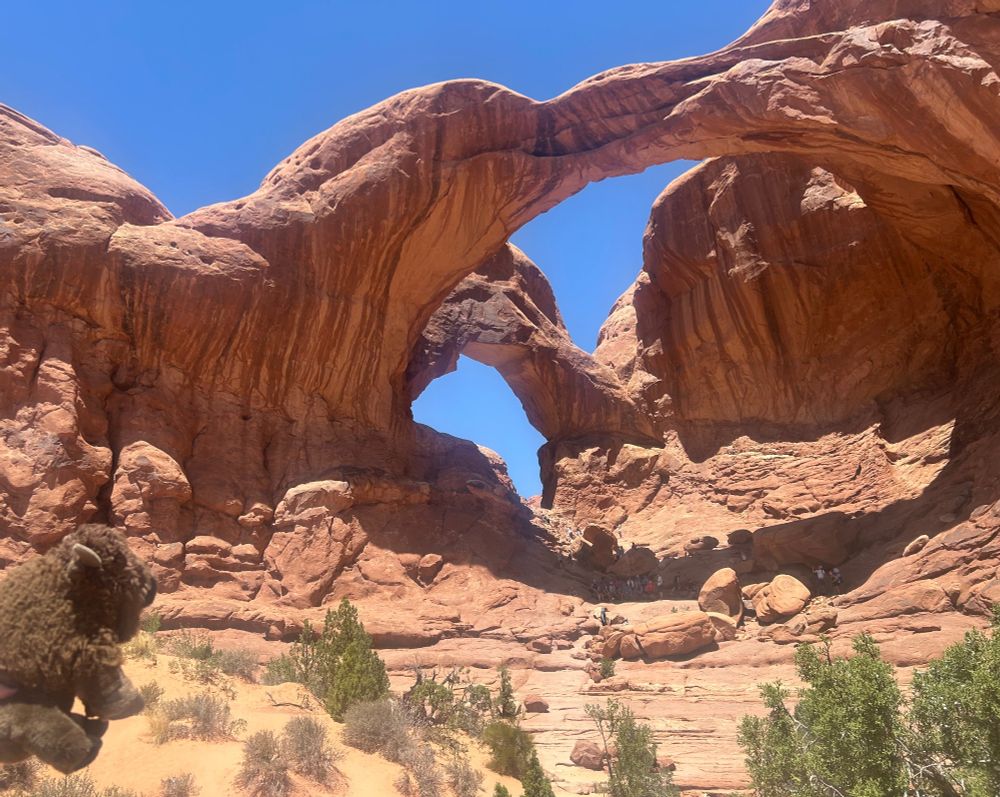 Rochester looking at the Double Arch: a rock formation in which two huge stone arches meet on the left, one closer to the camera and one extending back away from it.