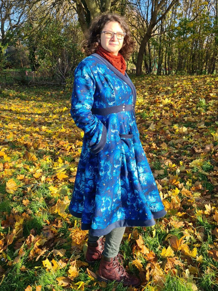 Side profile view of a dress length coat in fleecy galaxy fabric with a cross front fastening 