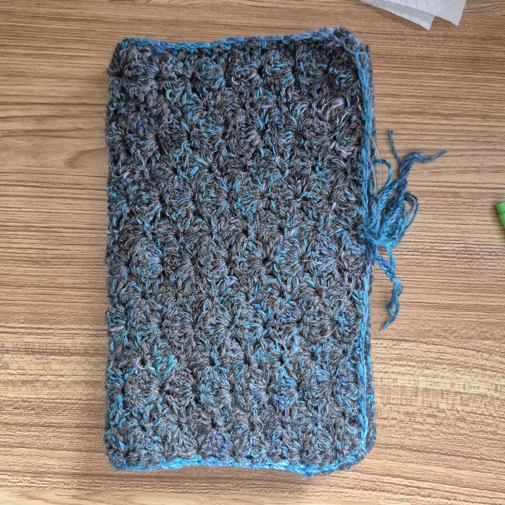 A blue and grey crocheted case, folded in half like a book
