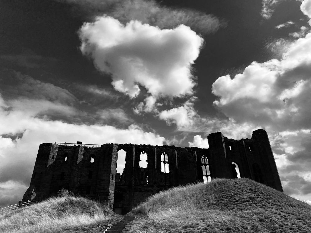 Silhouette of the Great Hall at Kenilworth Castle from below at the base of Kings Mound. Black and white image against a moody cloudy sky emphasising the beauty of the C14th windows. 