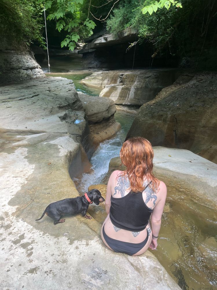 redhead woman with her black mini dachsund sitting in front of small waterfalls 