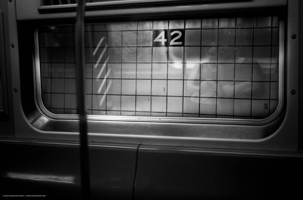 A photo of the window of a subway car. Outside of the window is the number 42 in wall tiles. 
