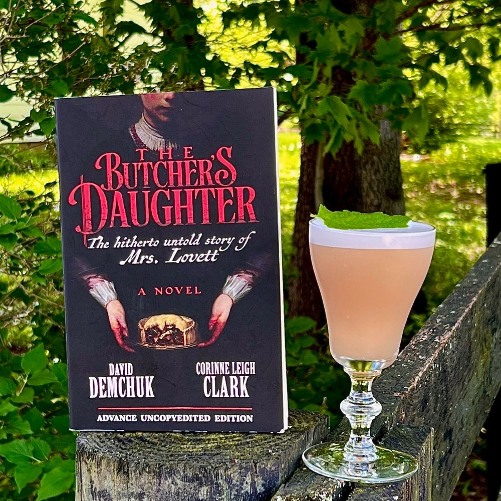 THE BUTCHER’S DAUGHTER by David Demchuk & Corinne Leigh Clark on a fence post in the shade along with a blush colored drink garnished with a lemon balm leaf. 
