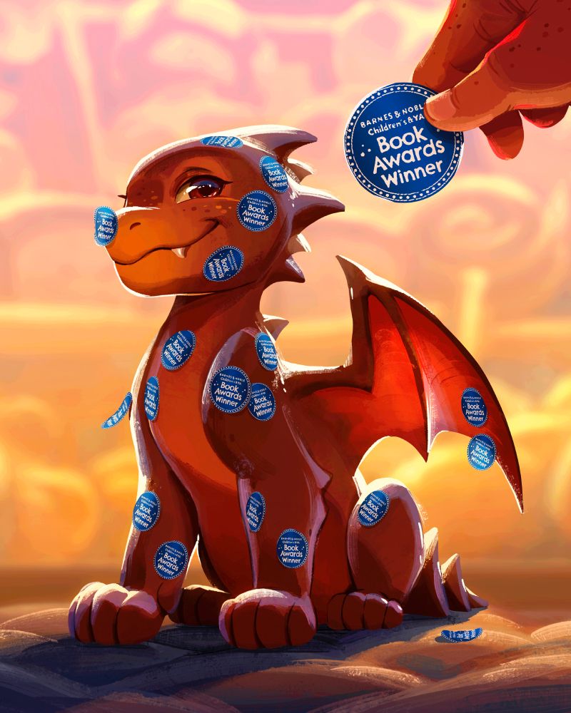 Ember the little red dragon from the book “the bakery dragon” sitting in front of a bakery window on cobblestone. He is covered in blue stickers that say “Barnes and Noble Children and YA Book Awards”