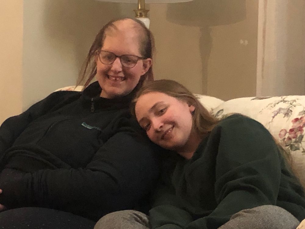 One teen girl leaning her head on the shoulder of an adult woman. Both as smiling and sitting on a couch.