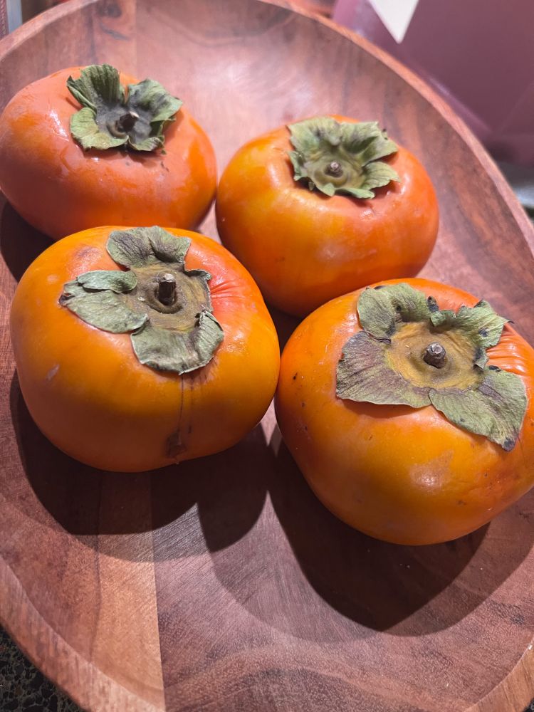 Four persimmon fruits on an oval wooden platter