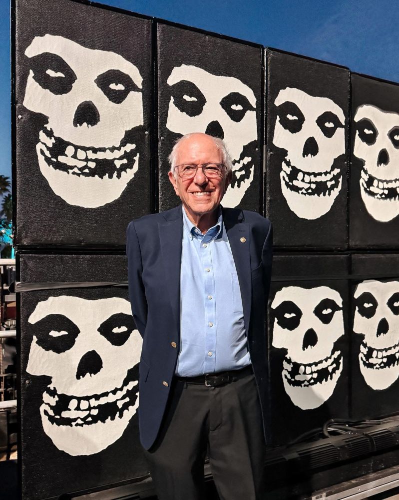 A smiling picture of Bernie Sanders at Coachella in from of the Misfits punk band logos 