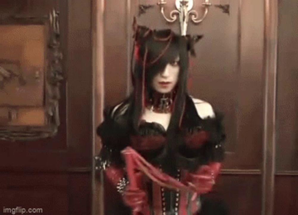 a woman in a gothic costume is holding a red whip in her hand .