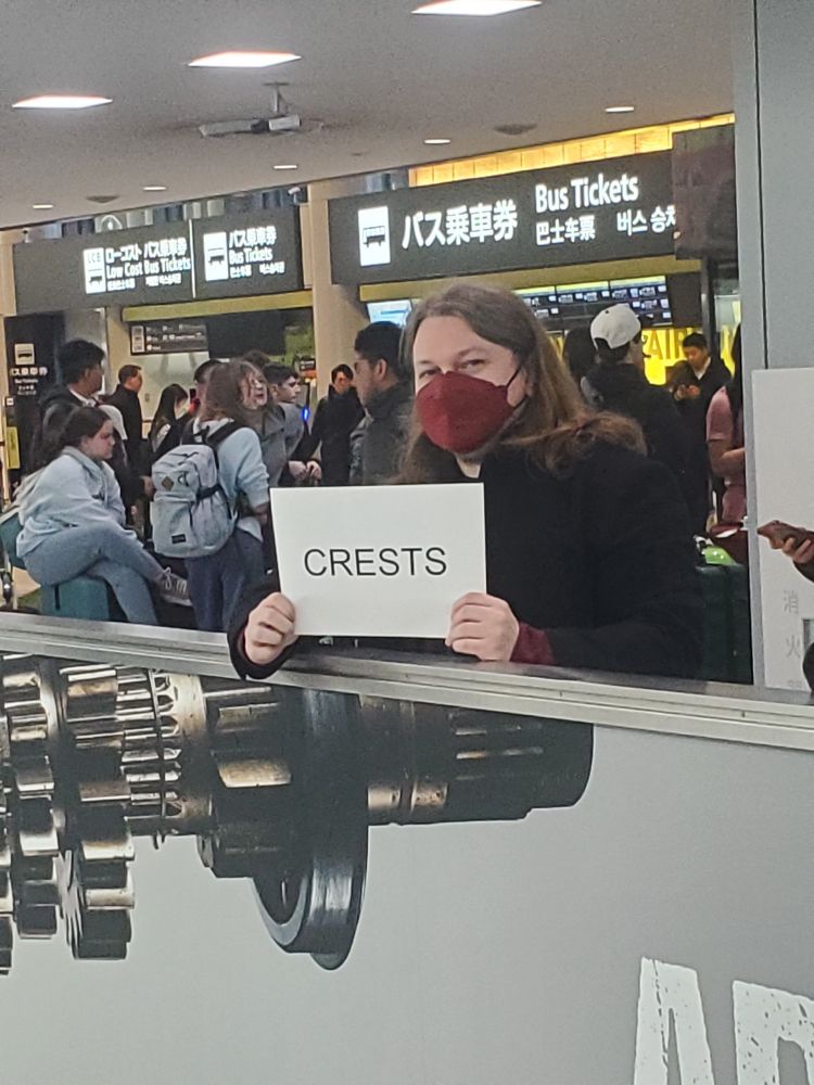Me standing at the international arrivals area of Narita airport holding a sign reading "CRESTS"