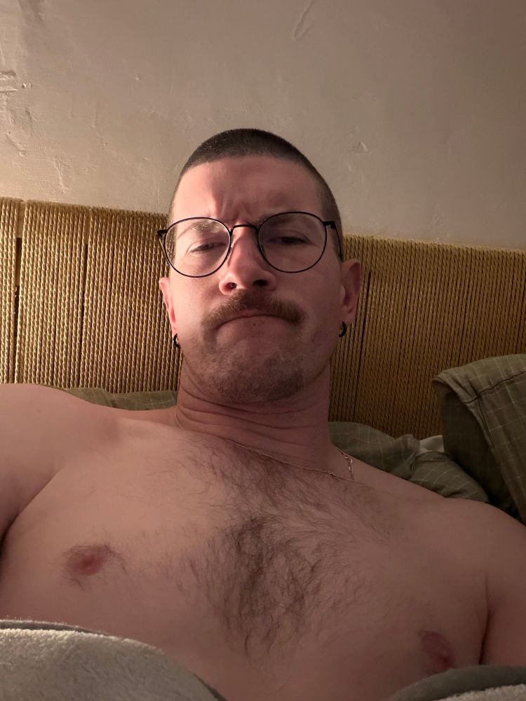 A man lying in bed with his full nipples out like a slut